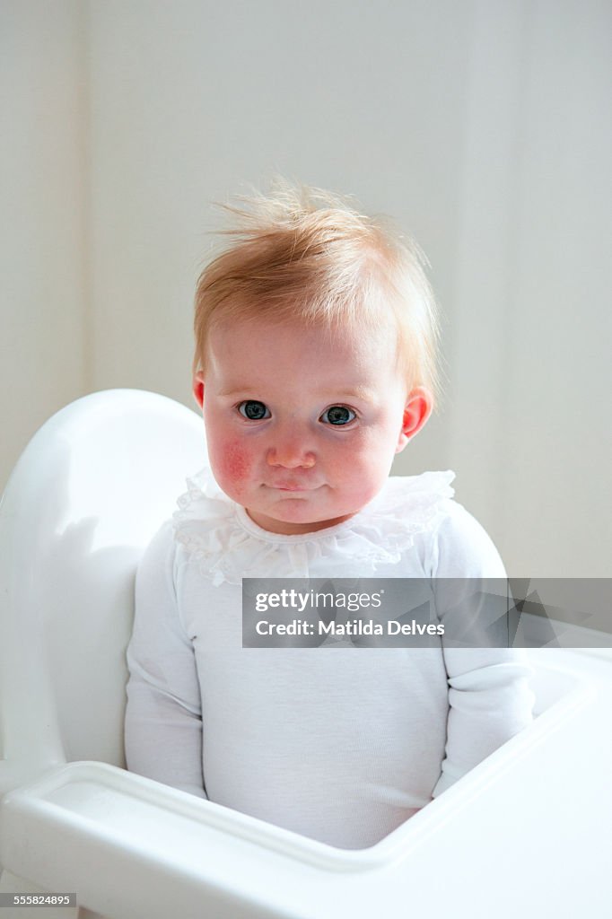 One year old baby girl sitting in a high chair