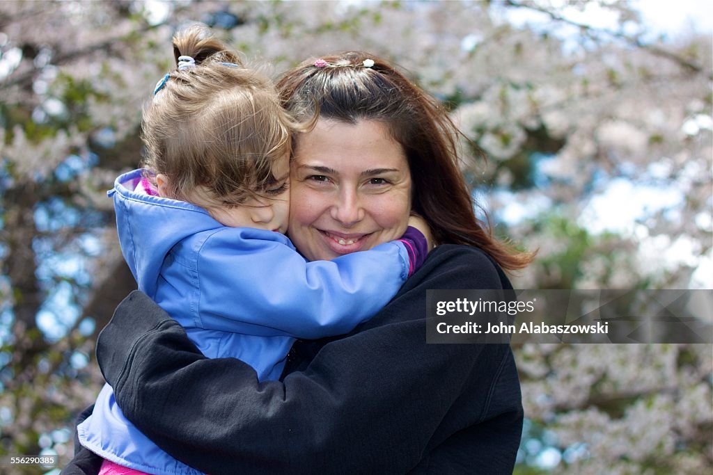 Mother and daughter hugging near cherry blossoms