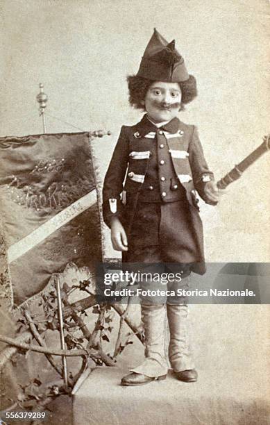 Child in masked as a "Raw Recruit" poses for a funny portrait. Photography sepia toning, Italy 1888.