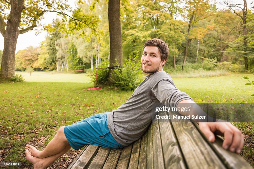 Portrait of barefoot young man sitting on park bench