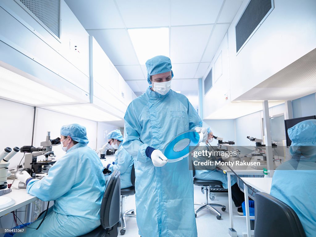 Electronics worker in clean room holding silicon wafer