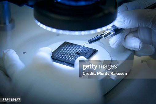 Electronics worker checking small electronic chips in clean room laboratory, close up Electronics worker checking small electronic chips in clean room laboratory, close up