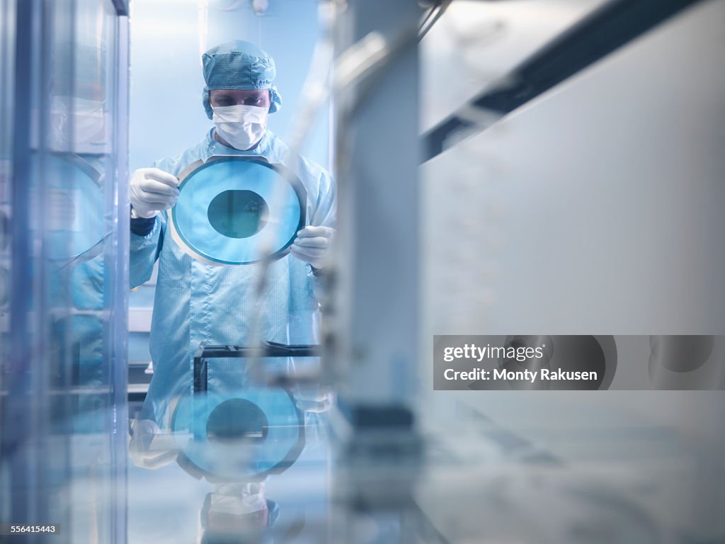 Electronics worker holding silicon wafer by cutting machine in clean room