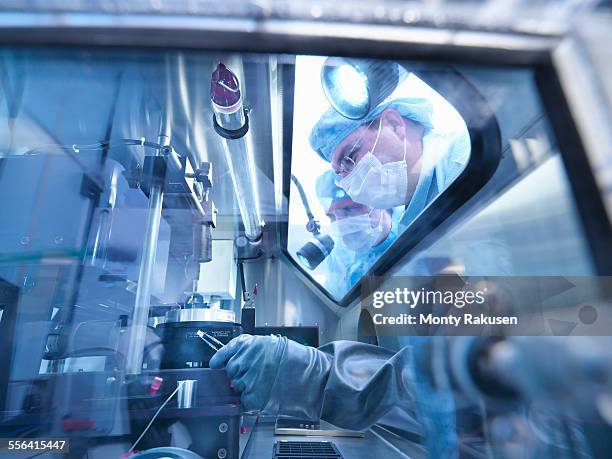 electronics workers looking into sealed work station window in clean room laboratory - cleanroom stockfoto's en -beelden