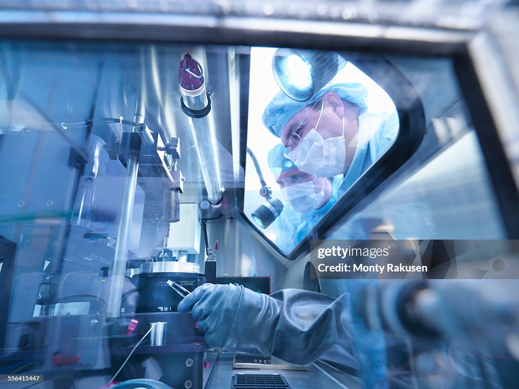 Electronics workers looking into sealed work station window in clean room laboratory