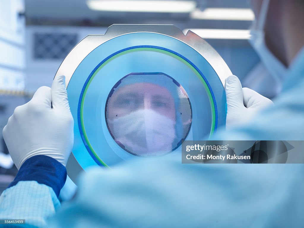 Electronics worker reflected in silicon wafer in clean room laboratory