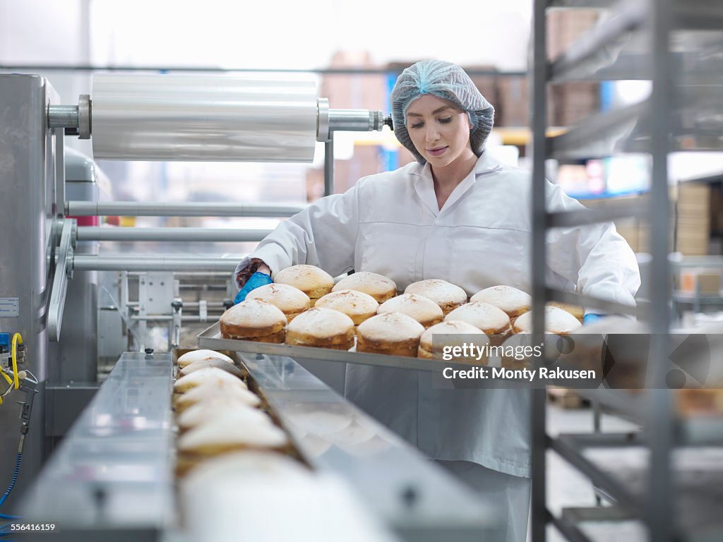 Female baker putting cakes on packaging line in cake factory