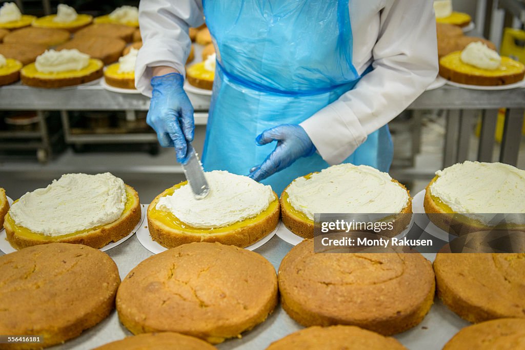 Female worker spreading filling on cakes in cake factory, close up