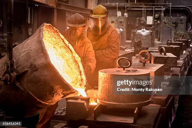 two workers pouring molten metal from flask in foundry - molten stock pictures, royalty-free photos & images
