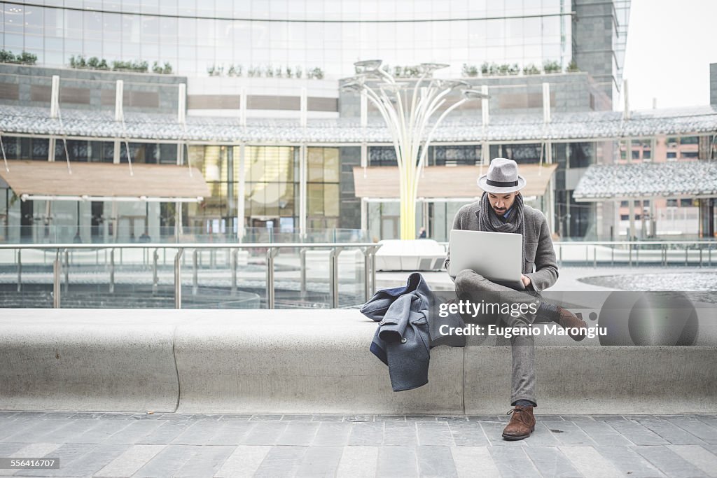 Businessman sitting on wall using laptop