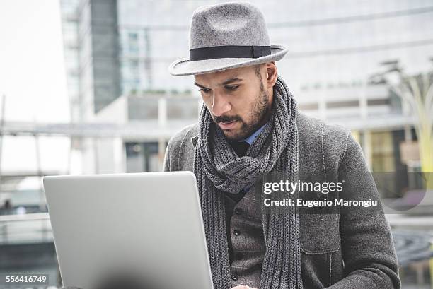 businessman sitting outside office using laptop - sombrero fedora fotografías e imágenes de stock