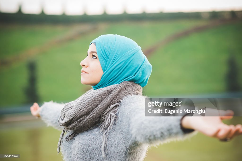 Young woman in park with arms open wearing turquoise hijab