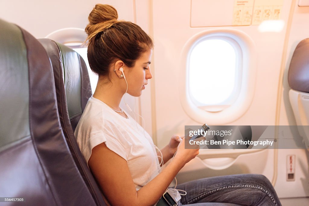 Young woman on airplane choosing music on smartphone