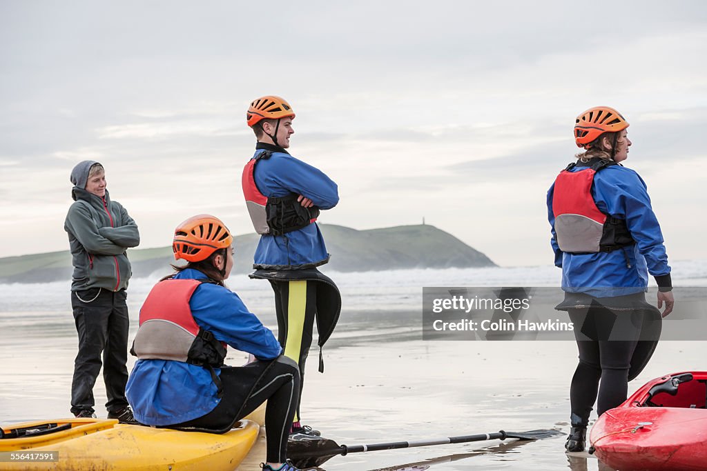Four people on beach with kayaks, Polzeath, Cornwall, England