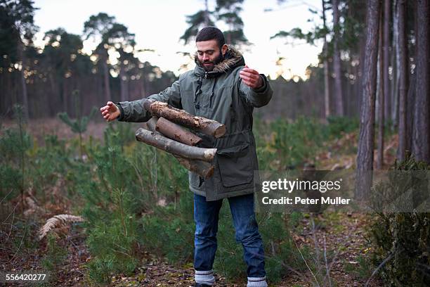 young man dropping logs for campfire in forest - traditional parka stock pictures, royalty-free photos & images