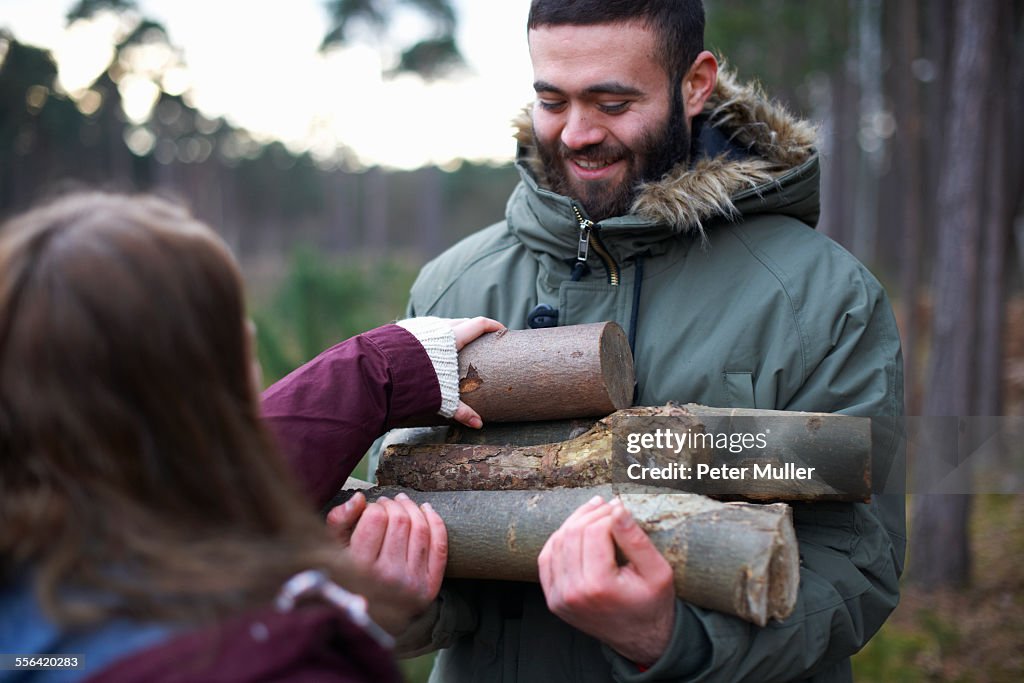 Young hiking couple collecting logs for campfire in forest