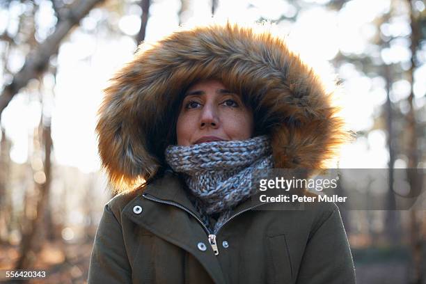 portrait of mature woman wearing fur hood and scarf in forest - parka cappotto invernale foto e immagini stock