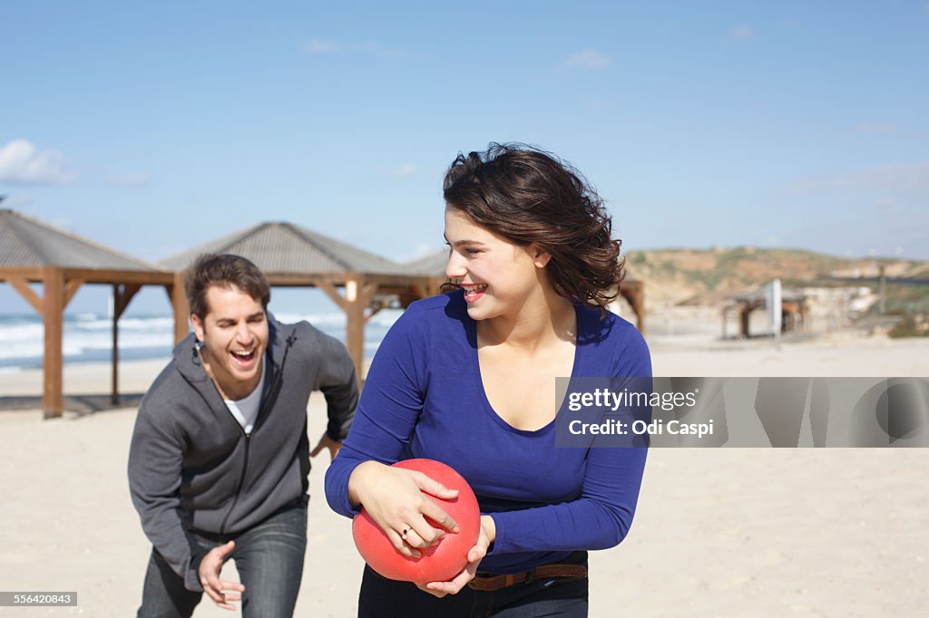 Young couple running with ball on beach, Tel Aviv, Israel