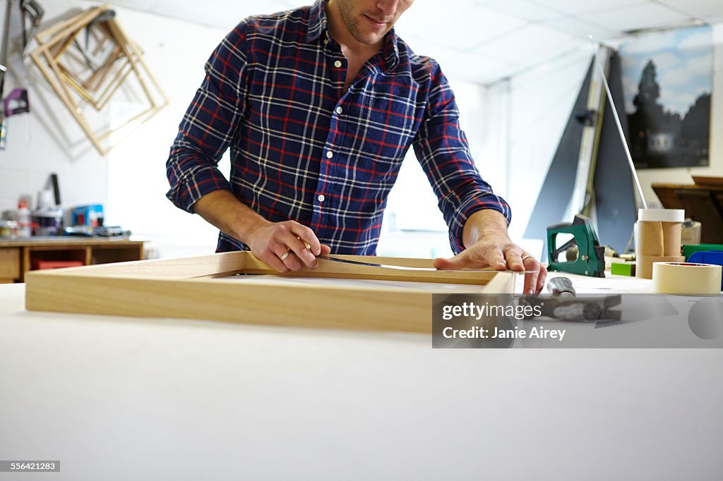 Mid adult man measuring frame on workbench in picture framers workshop