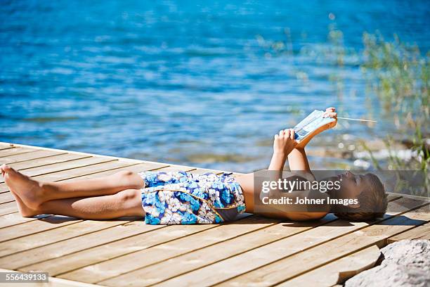 boy reading book at water - paperback stock pictures, royalty-free photos & images