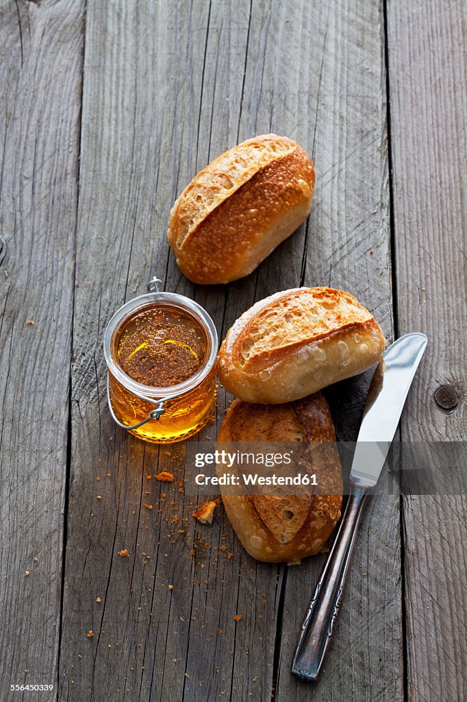Three bread rolls, glass of honey and a knife on grey wood