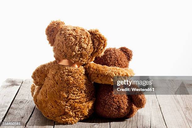 two teddy bears, arm on shoulder, back view on wood - teddybär stock-fotos und bilder