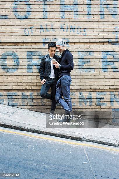 China, Hong Kong, gay couple at house wall looking on cell phone