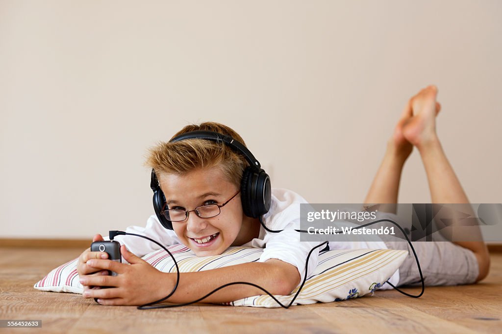 Smiling boy with MP3 Player and headphones lying on wooden floor