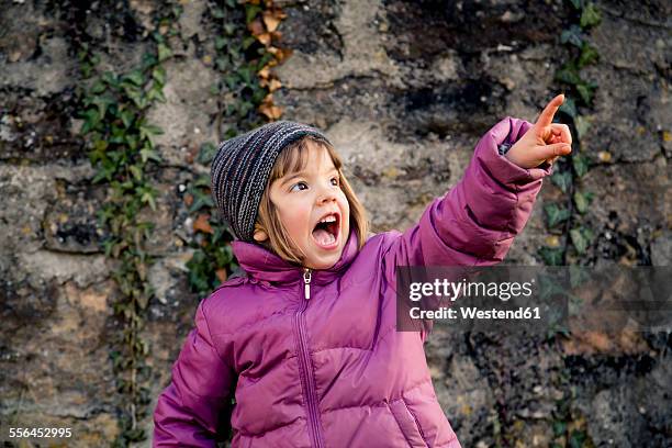 excited girl wearing woolly hat and pink winter jacket pointing at something - pink coat 個照片及圖片檔