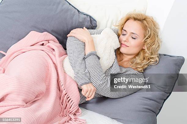 woman lying on couch with hot water bottle - wärmflasche stock-fotos und bilder