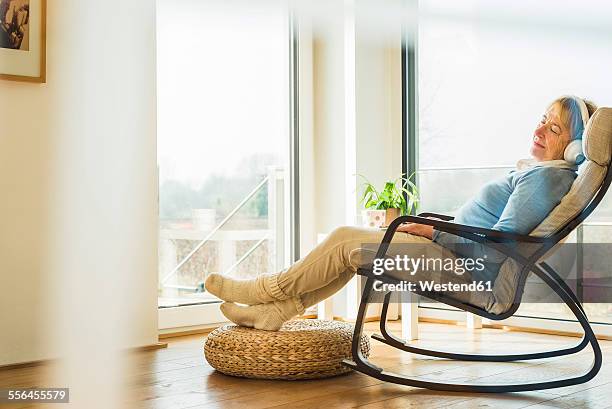 senior woman at home relaxing with headphones - schaukelstuhl stock-fotos und bilder