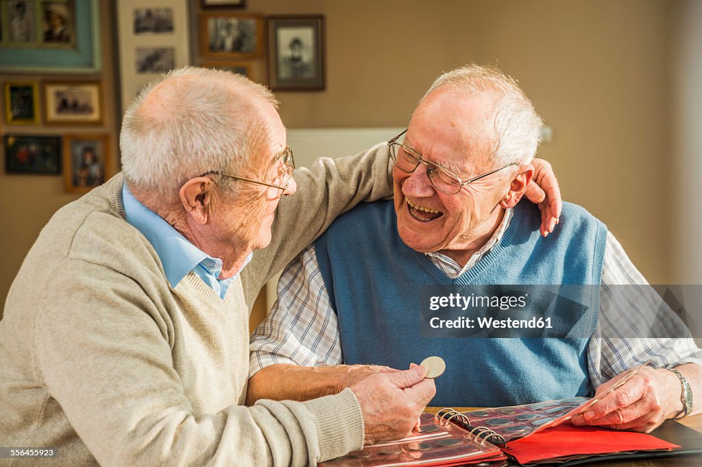 Two happy senior friends with coin album