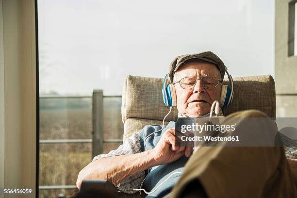 senior man at home relaxing with headphones - smartphone musik stock-fotos und bilder