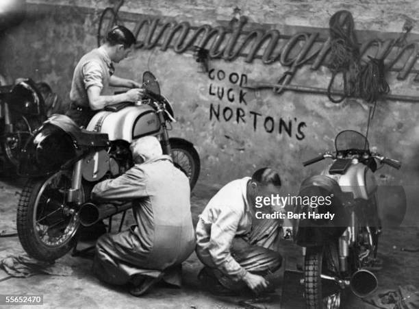 Mechanics tending to the Norton motorbikes which will be ridden in the Tourist Trophy Races on the Isle of Man, 9th June 1950. On the right is number...