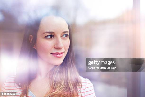 young woman gazes thoughtfully through window - reflexión fotografías e imágenes de stock