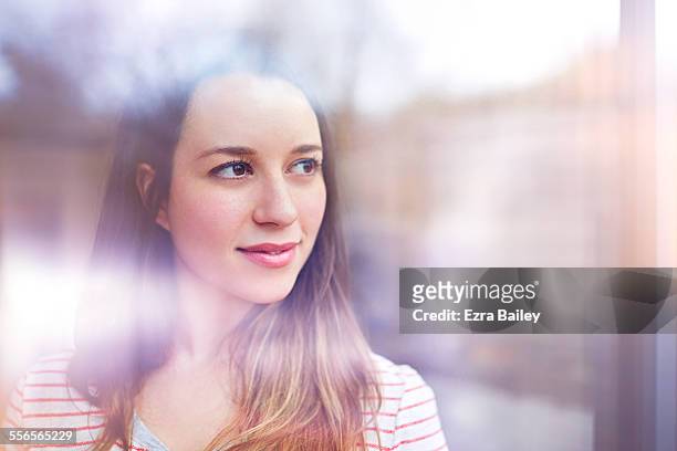young woman gazes thoughtfully through window - contemplation stock pictures, royalty-free photos & images