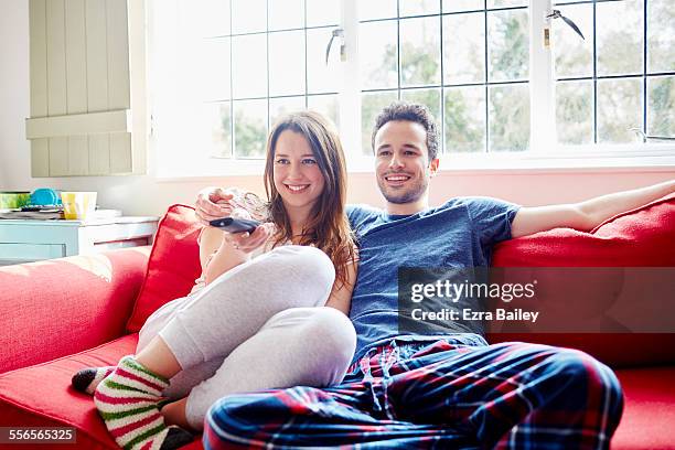 young couple relax on sofa watching tv - couple sitting stock pictures, royalty-free photos & images