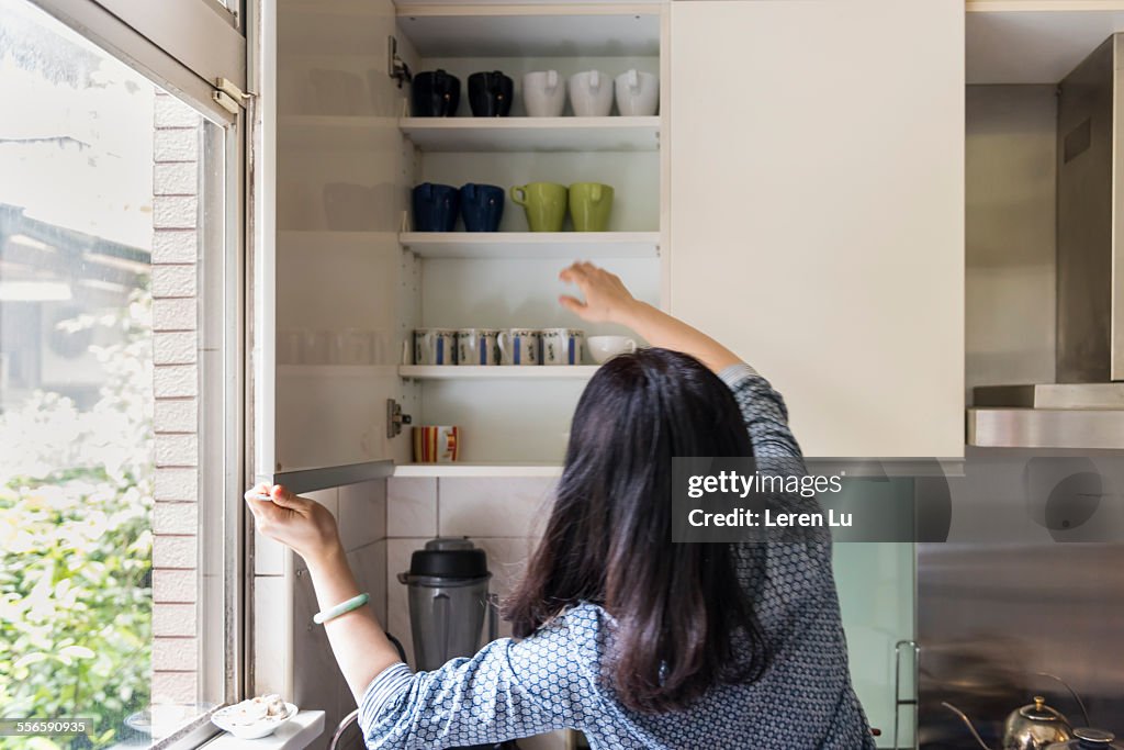 Woman taking cups out from shelf