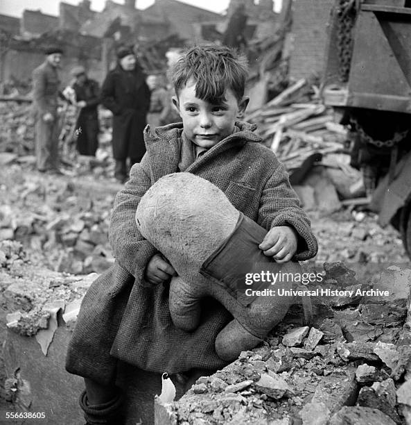 Abandoned boy holding a stuffed toy animal amid ruins following German aerial bombing of London during the Blitz of World War two.