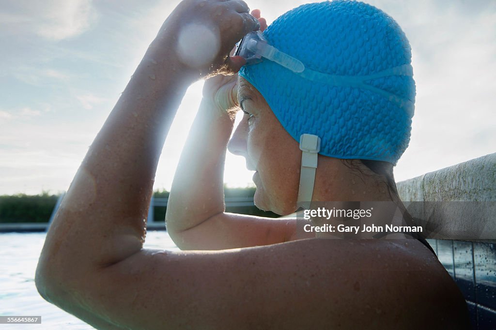Female swimmer in pool, pulling goggles down.