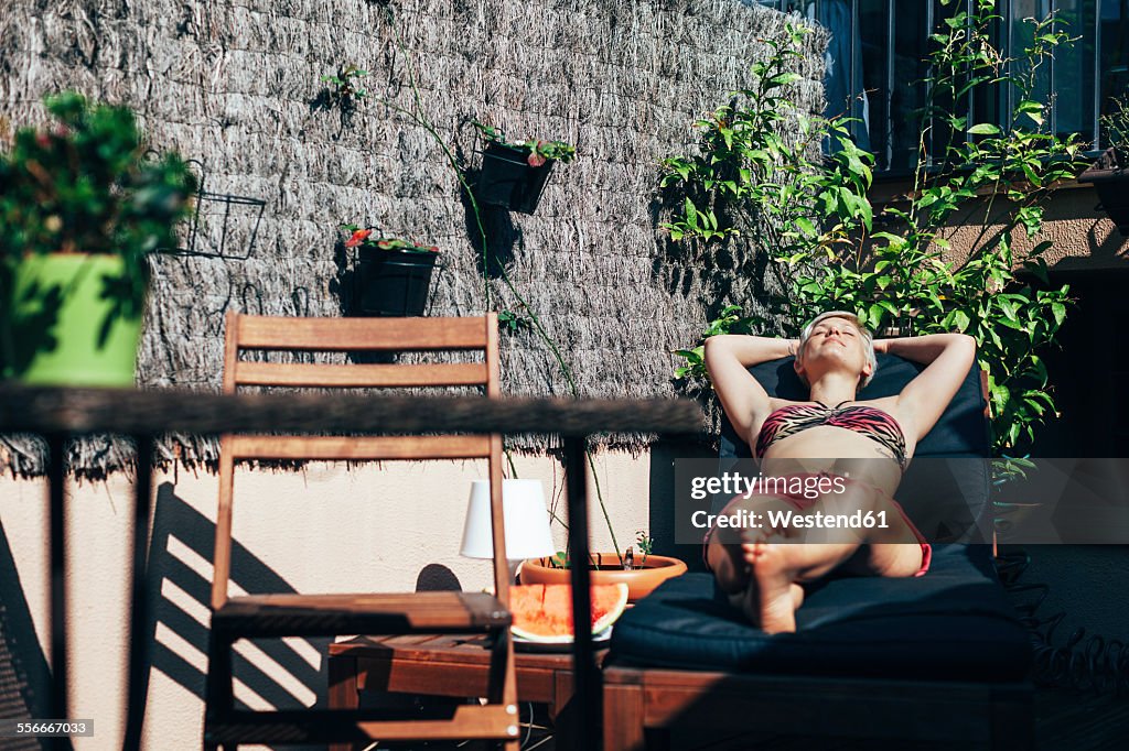 Young woman sunbathing on deck chair on her terrace