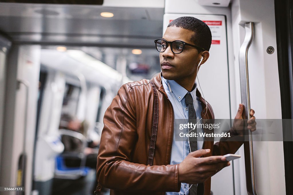 Businessman with smartphone and earphones hearing music on the subway train