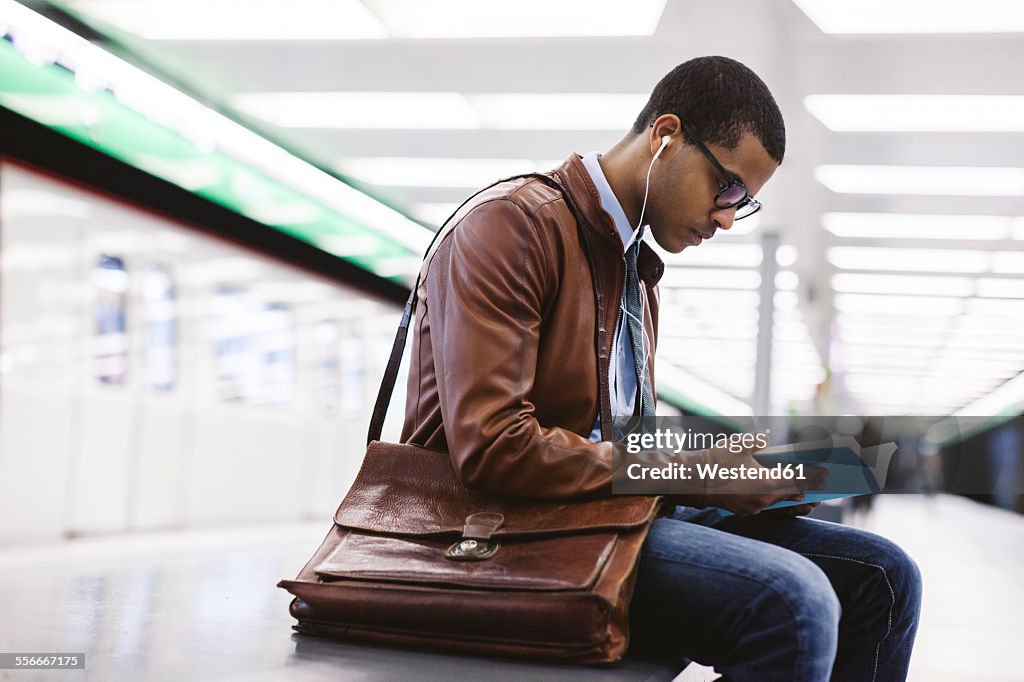 Spain, Barcelona, businessman sitting at underground station platform with book