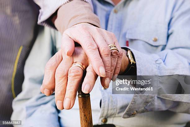 close-up of old man's and woman's hands resting on a cane - married stockfoto's en -beelden