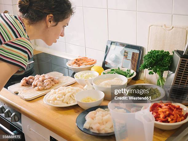 woman looking for pealla recipe on internet with ingredients in kitchen - recipe bildbanksfoton och bilder