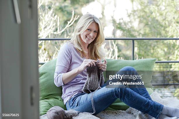 blond woman sitting on balcony knitting - knitting stock-fotos und bilder