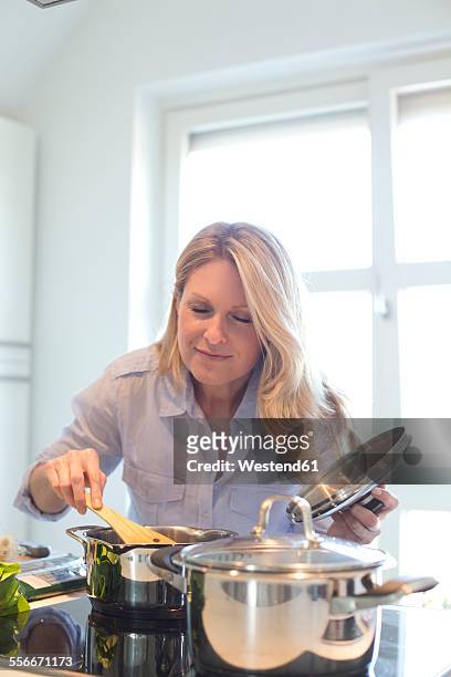 woman cooking in kitchen enjoying smell from cooking pot - older woman bending over stock pictures, royalty-free photos & images