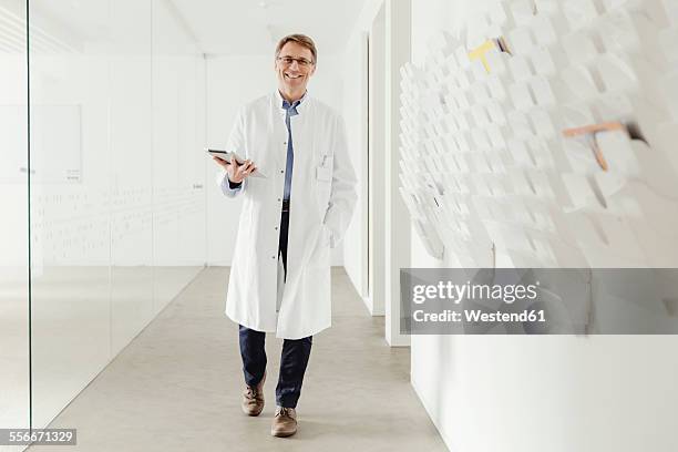 smiling mature man in lab coat walking in hallway - scientifique blouse blanche photos et images de collection