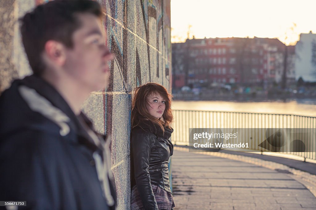 Germany, Berlin, teenage girl leaning at graffiti wall, boy blurred in foreground