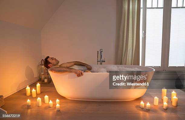 man relaxing in bathtub with lighted candles arround - bubbelbad stockfoto's en -beelden